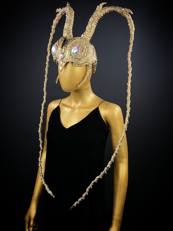 May include: A gold headpiece with a crown and two long, thin, gold strands. The crown has iridescent jewels and is decorated with gold beads.